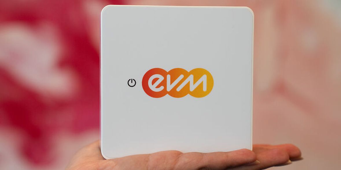 Eine Hand hält ein quadratisches, weißes Gerät mit dem farbigen „evm“-Logo