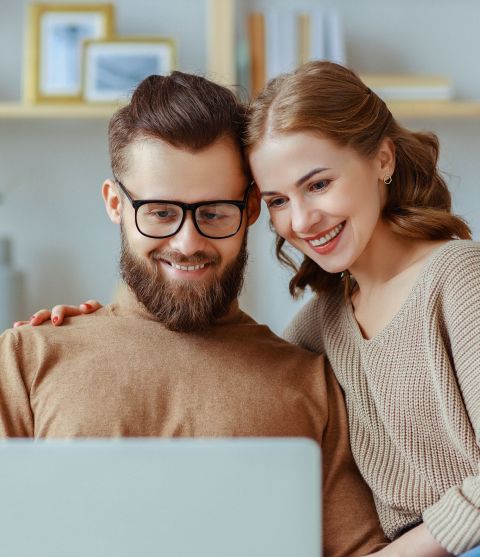 Ein Mann und eine Frau sitzen vor einem Laptop und lächeln freundlich.