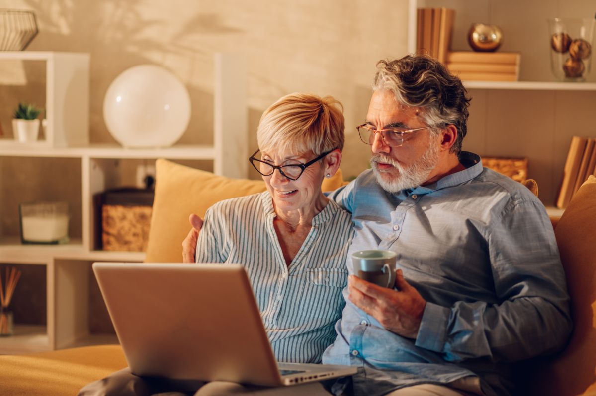 Senior couple using laptop while sitting on a couch at home Senior couple using laptop while sitting on a couch at home