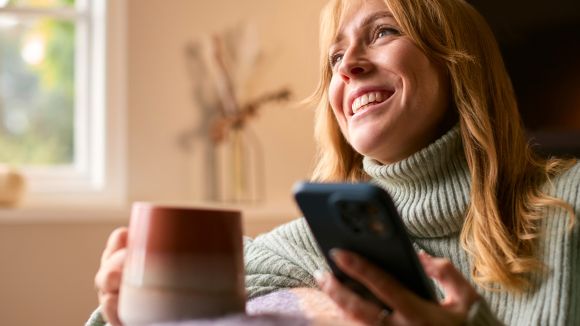 Woman At Home With Warming Hot Drink Of Tea Or Coffee In Cup Or Mug With Mobile Phone Woman At Home With Warming Hot Drink Of Tea Or Coffee In Cup Or Mug With Mobile Phone