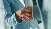 Nahaufnahme von zwei Personen die sich die Hand geben. Eine Person trägt einen blauen Blazer, die andere einen grauen Anzug.
