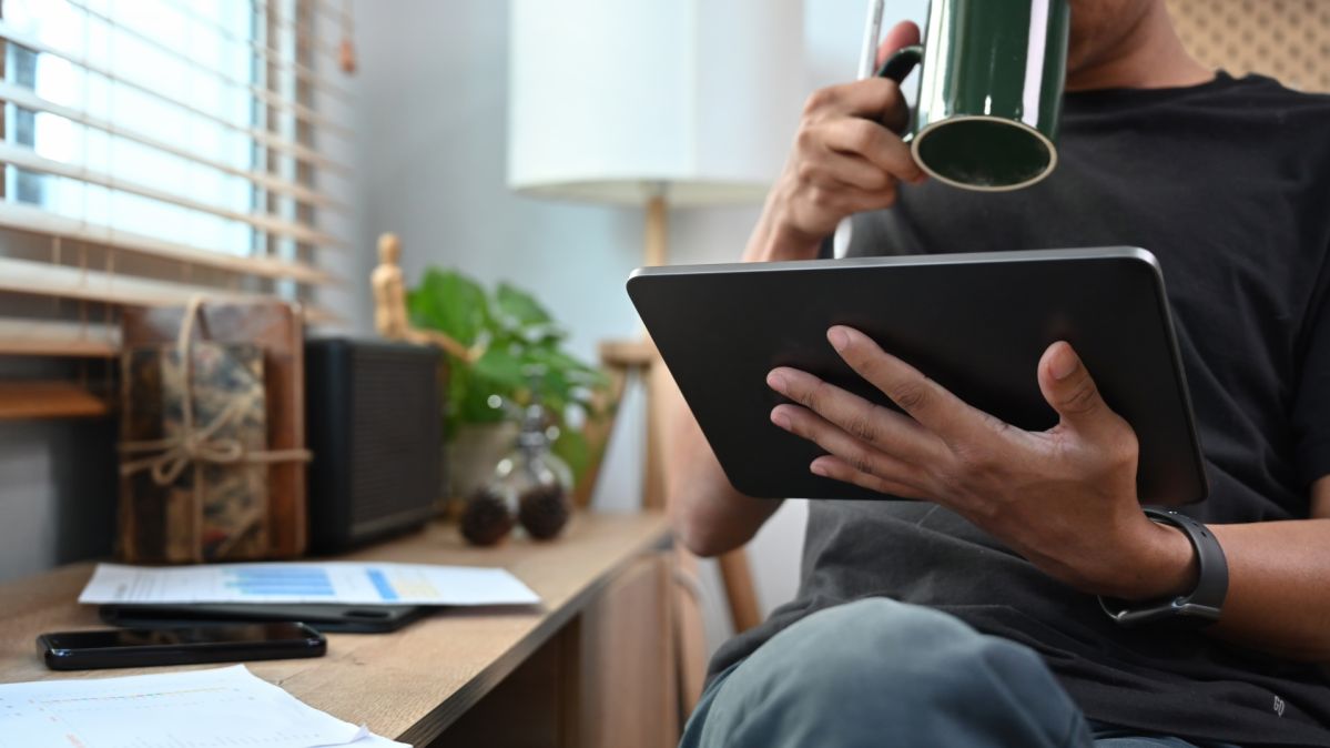 Man drinking coffee and analyzing graph stock market trading on digital tablet.