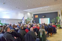 240124SDI1001 Ein Publikum sitzt in einem Saal. Vor ihnen steht ein professionell gekleideter Mann und präsentiert..
