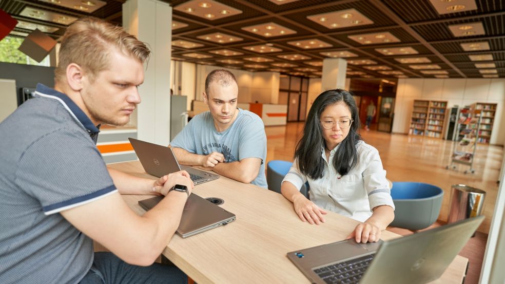 Drei Kolleginnen und Kollegen sitzen am Schreibtisch und führen ein Präsenzmeeting durch. 