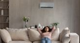 Eine Frau sitzt lässig auf einem beigen Sofa und hat ihre Arme hinter dem Kopf verschränkt. Über ihr befindet sich eine Klimaanlage.