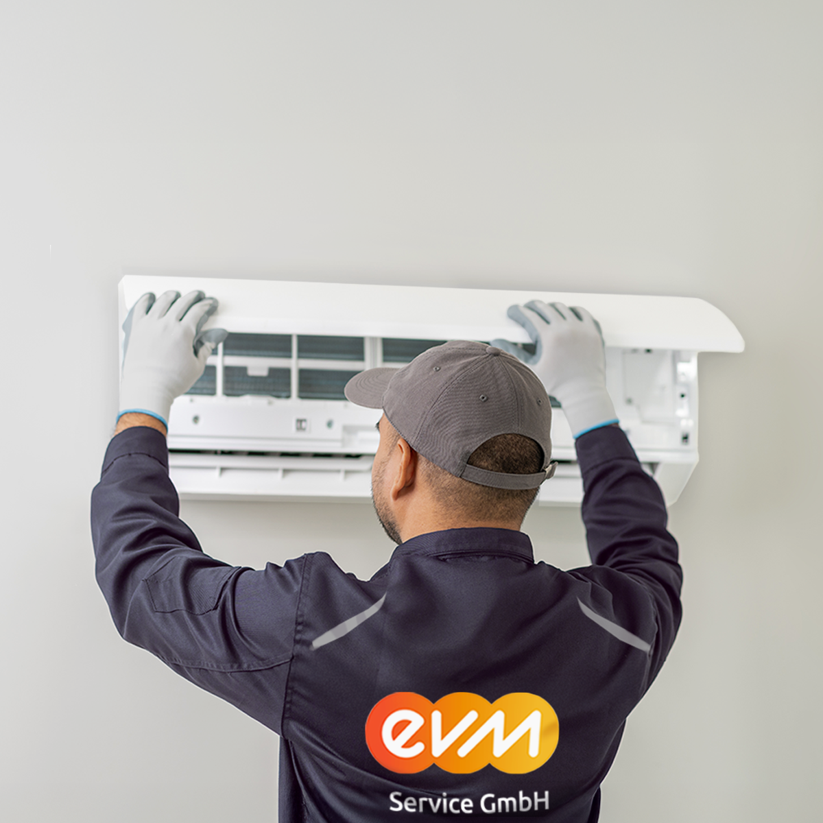 Ein Mann mit einer grauen evm Service GmbH Jacke mit orangenem evm Logo arbeitet an einer Klimaanlage.