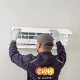Ein Mann mit einer grauen evm Service GmbH Jacke mit orangenem evm Logo arbeitet an einer Klimaanlage.