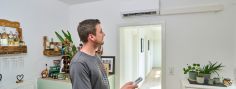 Mann steht im Wohnzimmer und bedient seine Klimaanlage