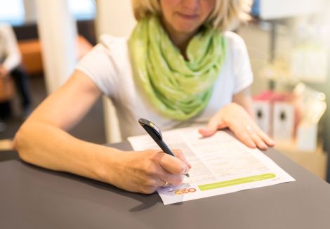 Eine Frau mit einem grünen Schal steht an einem Tisch und füllt ein evm Formular aus.