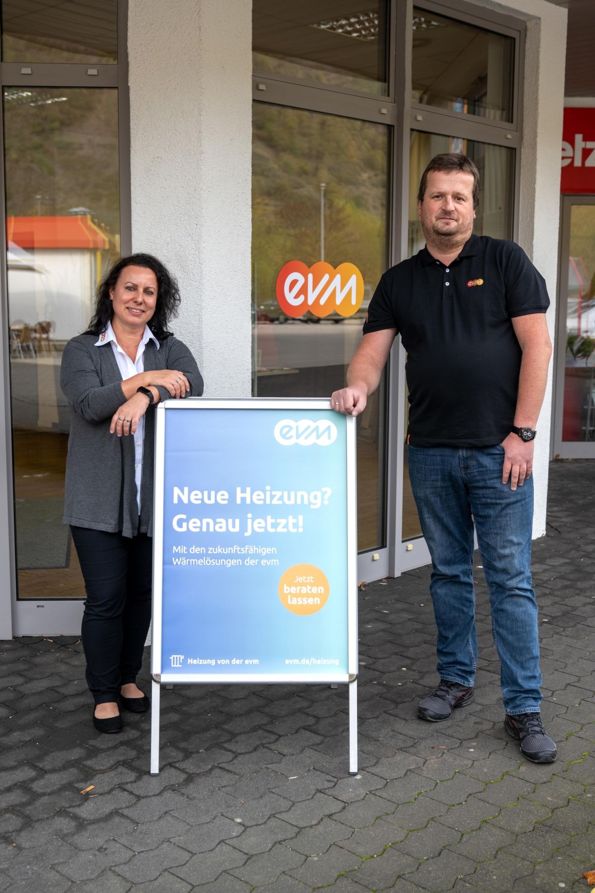 Eine Frau und ein Mann stehen vor einem evm Kundenzentrum. Sie stehen neben einem Plakatständer.