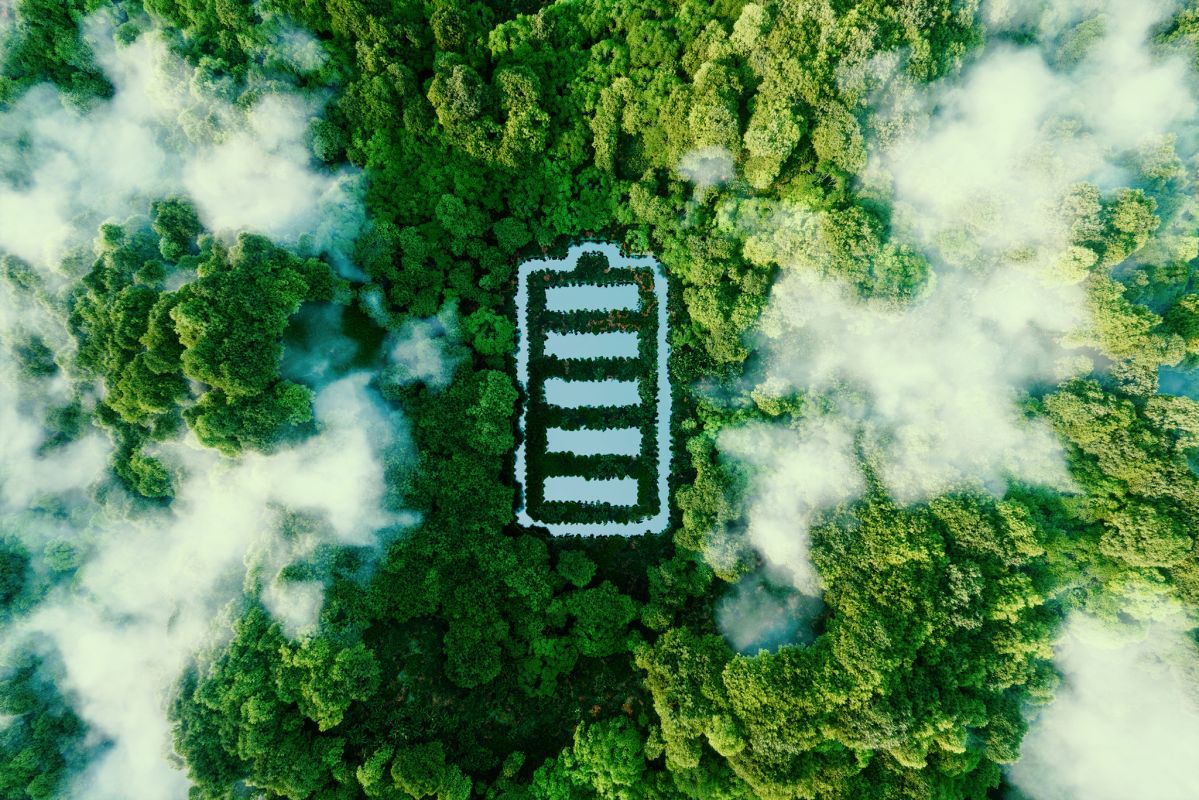 Ein großer, weißer Batterie-Umriss liegt auf einem dichten, grünen Waldboden. Wolken umgeben den Bereich, schaffen eine friedliche und natürliche Atmosphäre.