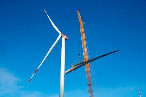 Neben einem Windrad steht ein Kran. Im Hintergrund ist ein blauer Himmel.
