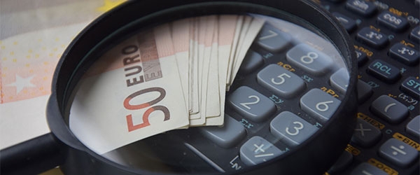 Eine Lupe liegt auf 50-Euro-Geldscheinen und einem Taschenrechner