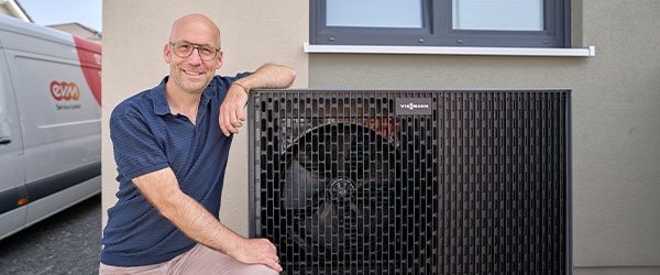 Thomas Schmitz kniet glücklich neben seiner neuen Wärmepumpe