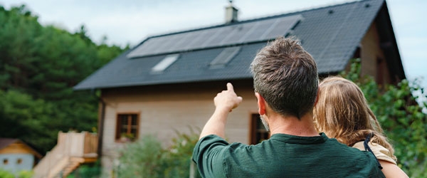 Vater und Kind schauen auf ihr Haus mit PV-Anlage