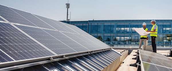 Zwei Installateure mit Warnwesten und Helm auf einem Dach neben Solarmodulen