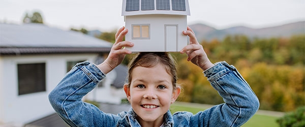 Fröhliches Mädchen hält Spielzeughaus mit Solaranlage