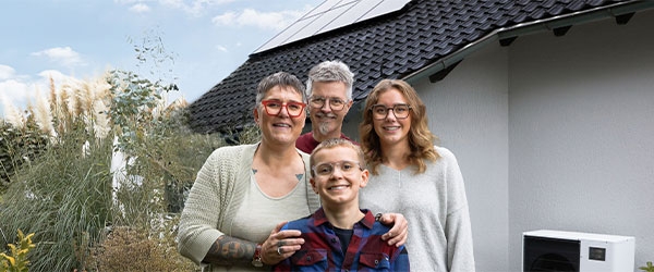 Familie Schnell-Mand im Garten, hinter ihnen eine Solaranlage und Wärmepumpe