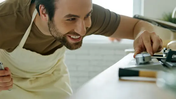 Ein Mann mit einer Kochschürze steht an einem Gasherd und dreht eine Herdplatte auf.
