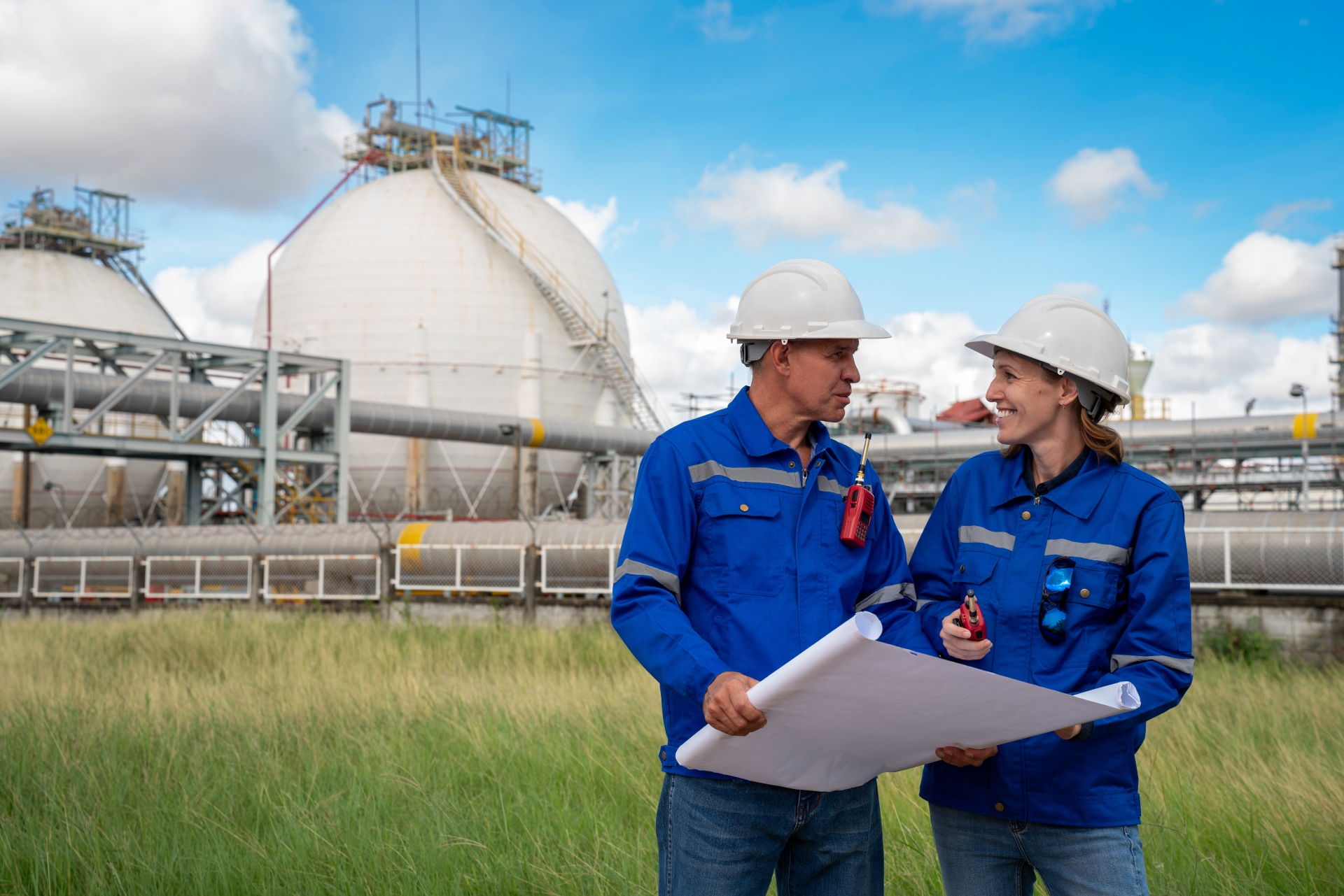 Gasspeicherumlage sinkt zum 01.07.2025 – profitieren Sie bereits automatisch davon? Diskussion eines Teams von Chemieingenieur:innen über Baupläne innerhalb einer Ölraffinerie und Gasanlage. Ein leitender Ingenieur trägt eine Sicherheitsweste und persönliche Schutzausrüstung (PSA) und arbeitet an einer petrochemischen Anlage