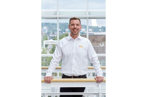 Ein Mann mit einem weißen evm Hemd steht an einer Balustrade und lächelt freundlich