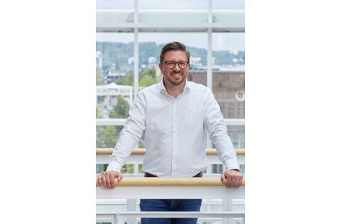 Ein professionell gekleideter Mann steht an einer Balustrade und lächelt freundlich