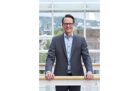 Ein professionell gekleideter Mann steht an einer Balustrade und lächelt freundlich