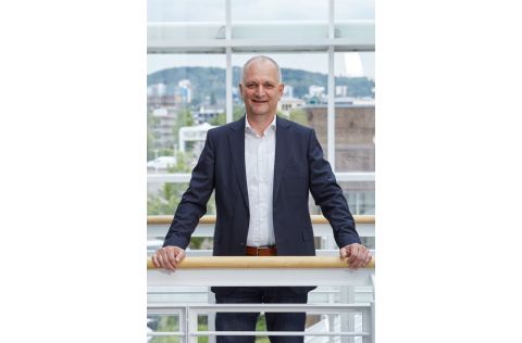 Ein professionell gekleideter Mann steht an einer Balustrade und lächelt freundlich