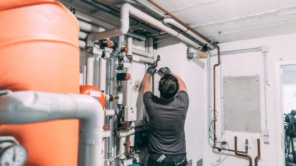 Einbau Wärmepumpe und PV Kunde Suwelack Ein evm Handwerker steht in einem Keller und arbeitet an einem Rohr.