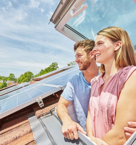 Solaranlage auf Schrägdach Ein Paar steht in einem Dachfenster und schauen raus. Auf dem Dach befindet sich eine Solaranlage.