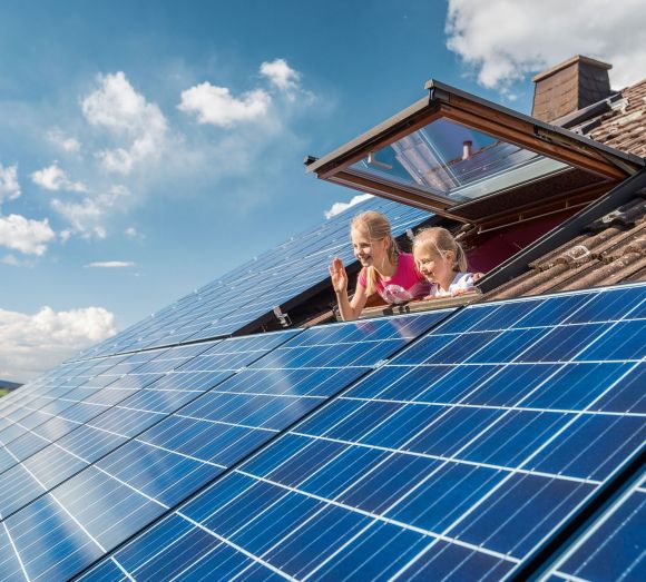 Kinder schauen aus einem Dachfenster auf die Solaranlage.