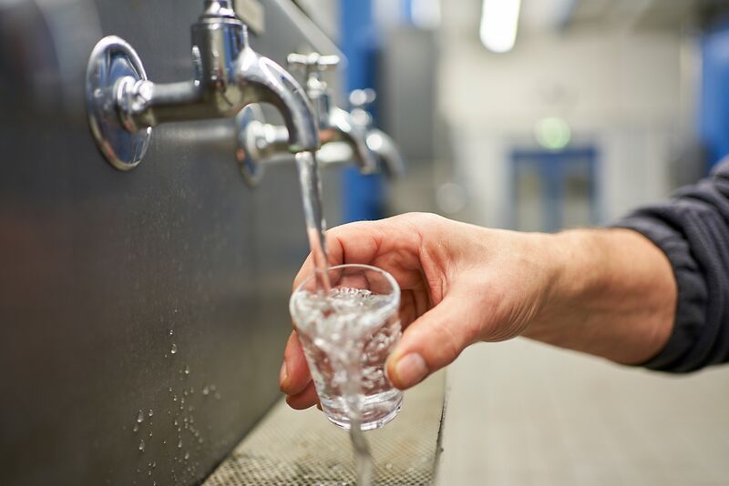 Eine Person hält ein Glas unter einen Wasserhahn.