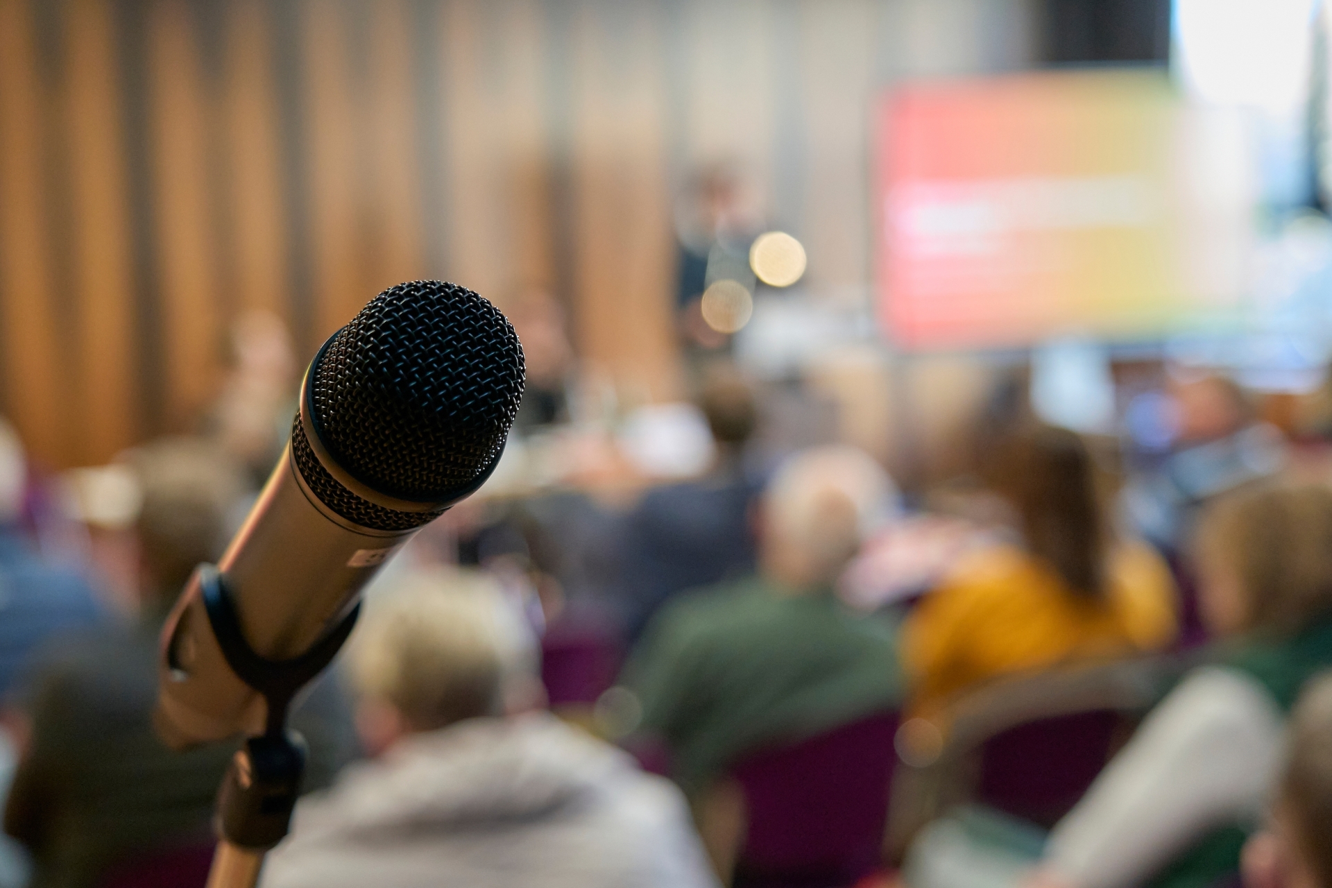 Ein Mikro ist scharf im Vordergrund. Der Hintergrund ist unscharf und zeigt einen Saal.