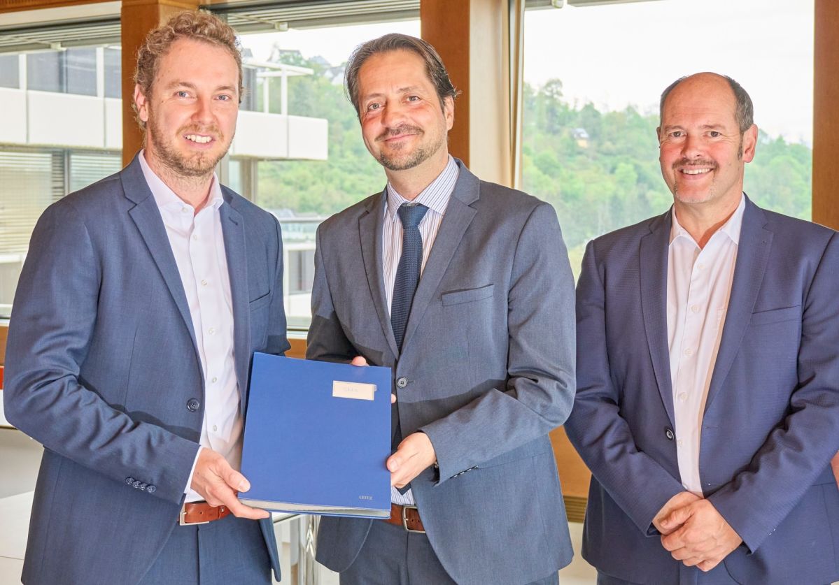 3 Männer lächeln freundlich in die Kamera und sind professionell gekleidet. Sie halten eine blaue Mappe in die Kamera.