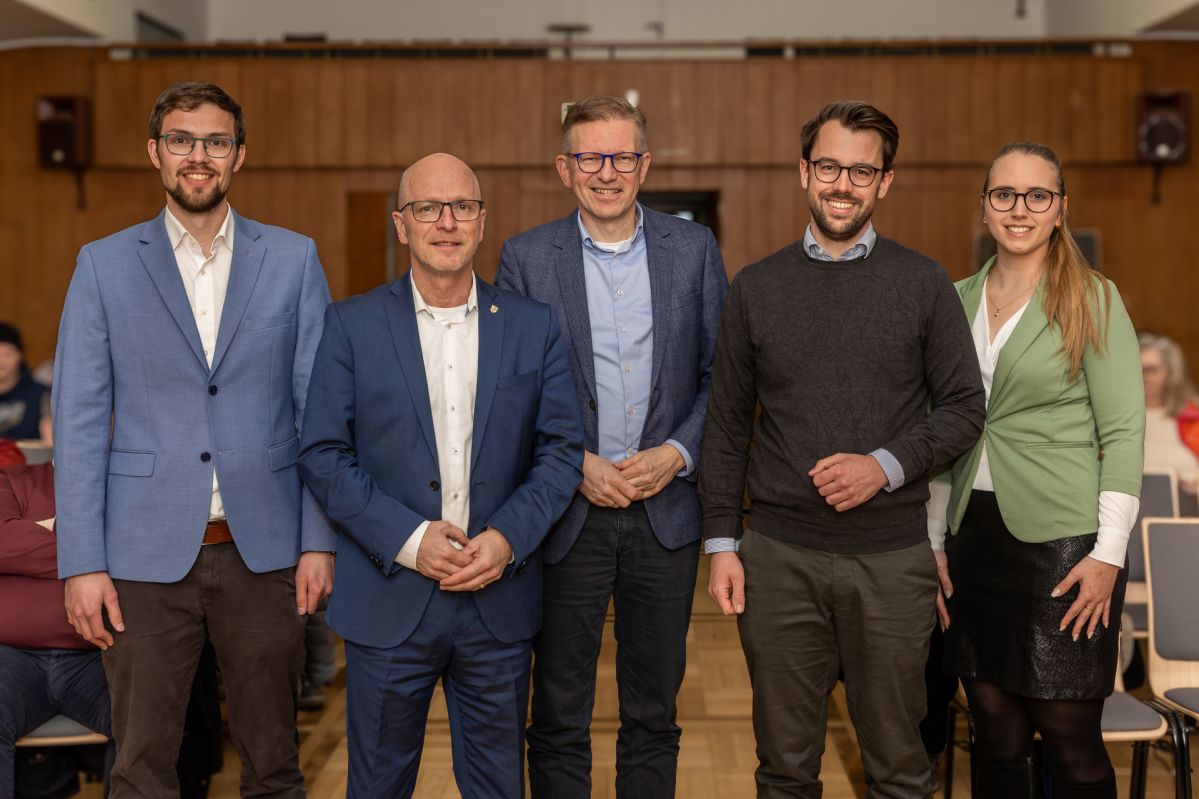 Vier Männer und eine Frau lächeln freundlich in die Kamera. Sie tragen alle eine Brille und sind professionell gekleidet.