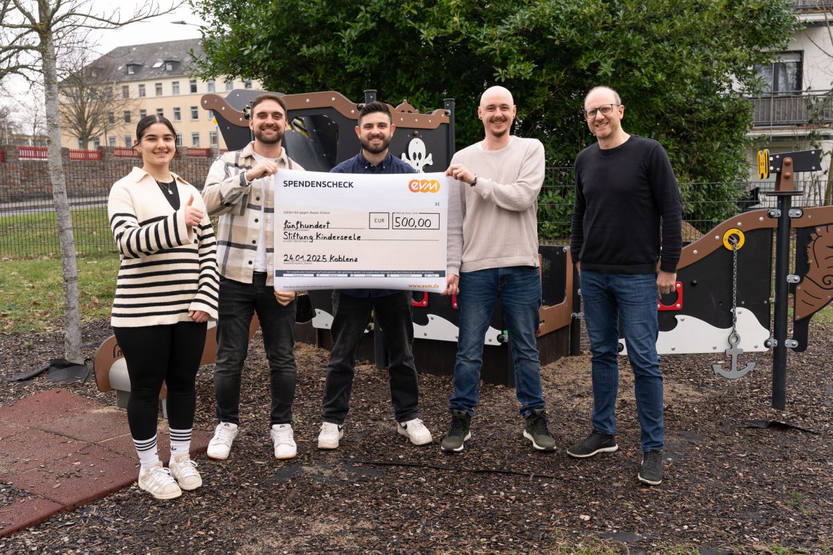 Spendenübergabe Azubis an ISA-Gruppe 4 Männer und eine Frau stehen freundlich lächelnd vor einem Spielplatz. Sie halten ein großes Plakat auf dem "Spendencheck evm" und der Beitrag von 500 Euro stehen.