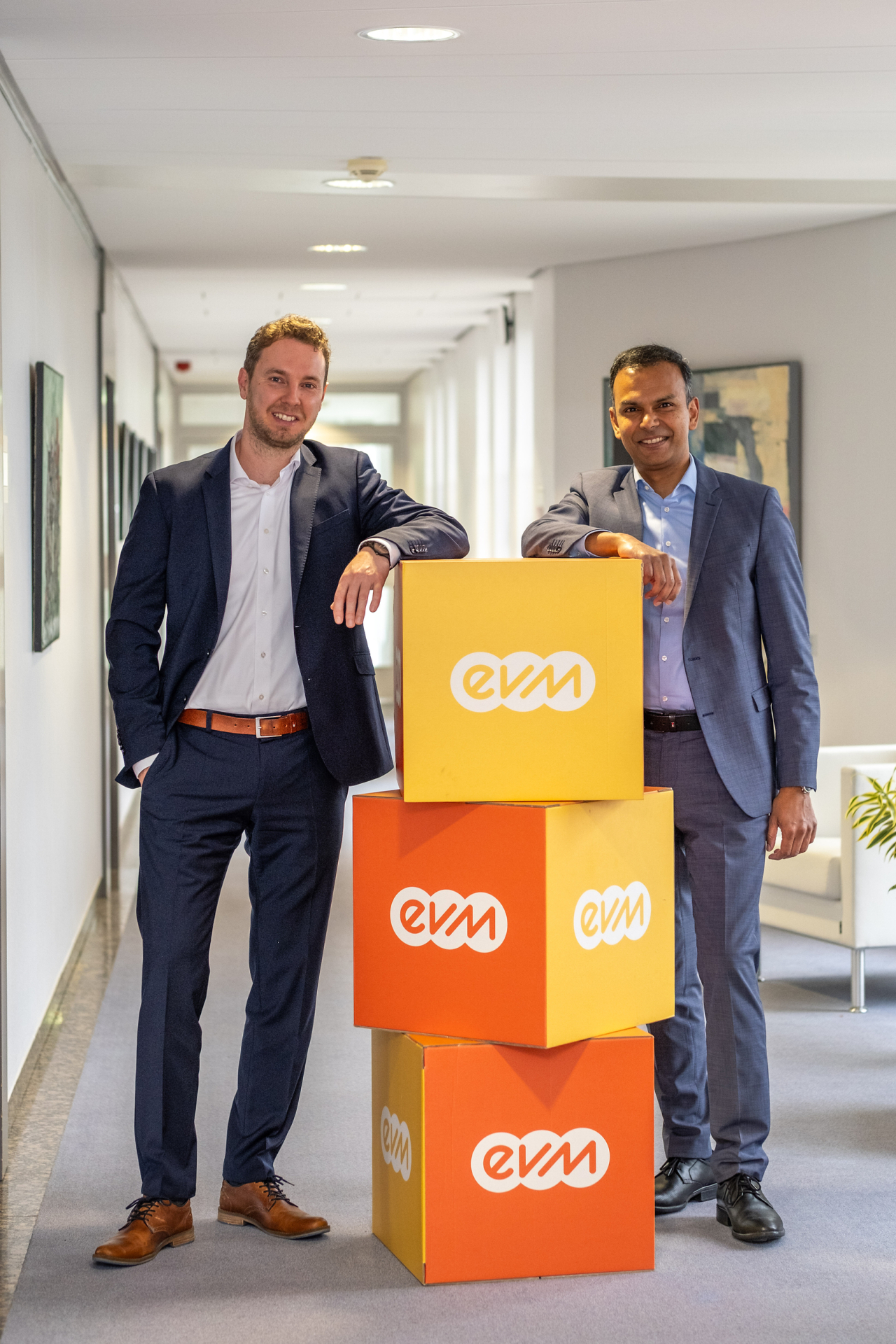 Zwei professionell gekleidete Männer stehen neben aufeinander gestapelten evm Würfeln.