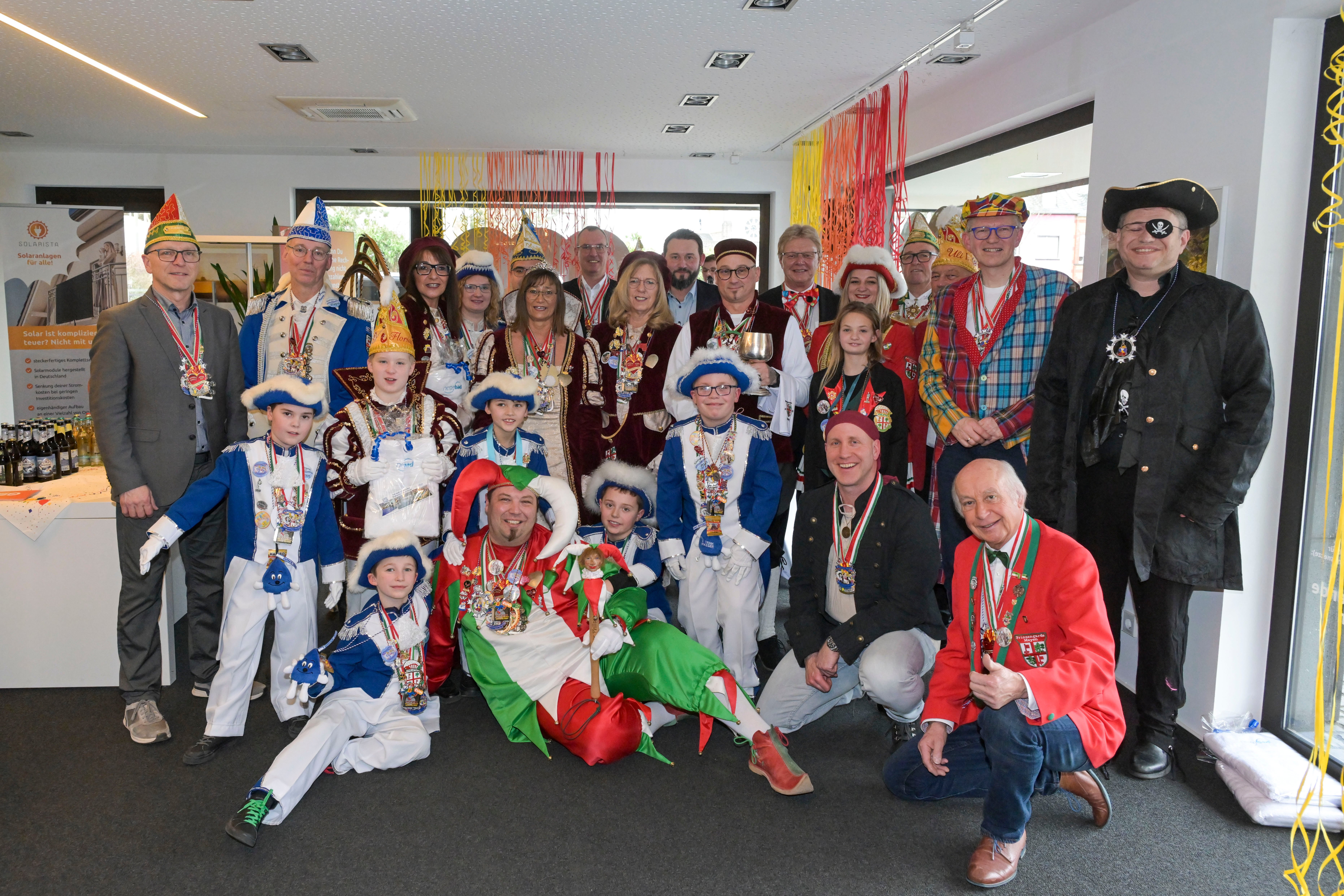 Eine große Gruppe von Karnevalisten steht in einem Raum und lächelt freundlich.