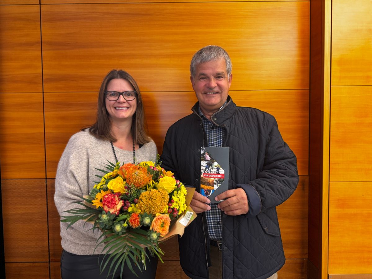 Zwei Personen stehen vor einer holzverkleideten Wand. Nicole Schröder von der evm übergibt einen Gutschein über 2.000 Euro von Fahrrad Franz an den glücklichen Gewinner Roland Goerke.