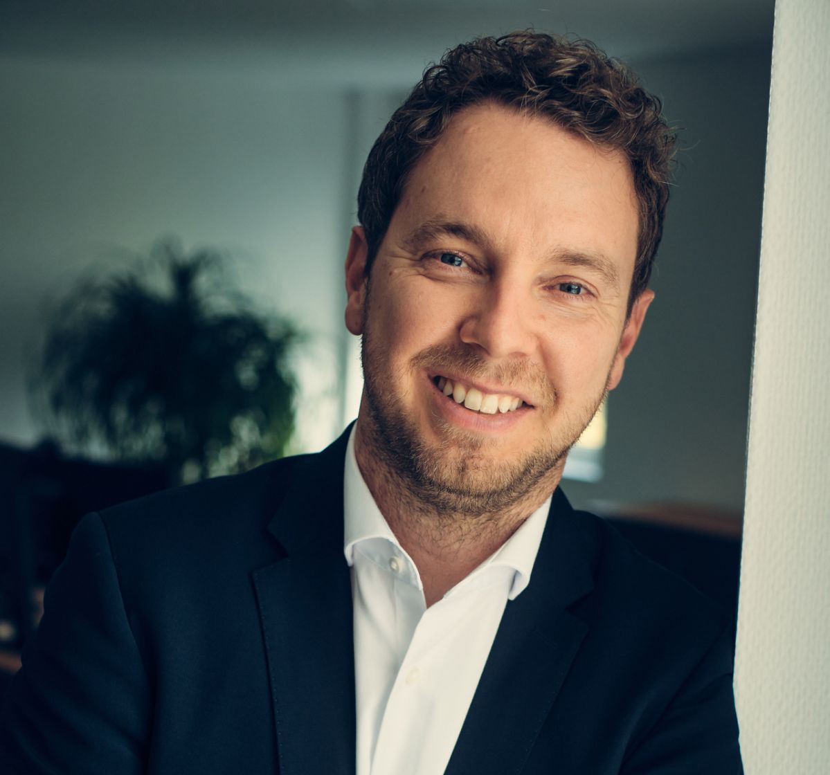 Christoph Hesse Ein professionell gekleideter Mann lehnt mit verschränkten Armen an einer Wand und lächelt freundlich.