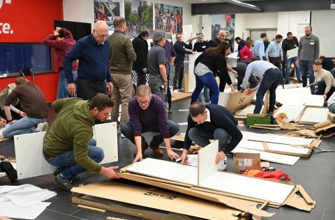 Viele Personen stehen in einem Raum und bauen weiße Ikea Regale auf.