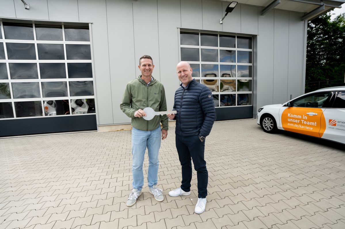 Lagereröffnung Cochem-06 Zwei Männer stehen vor einer Lagerhalle und halten einen großen Schlüssel.