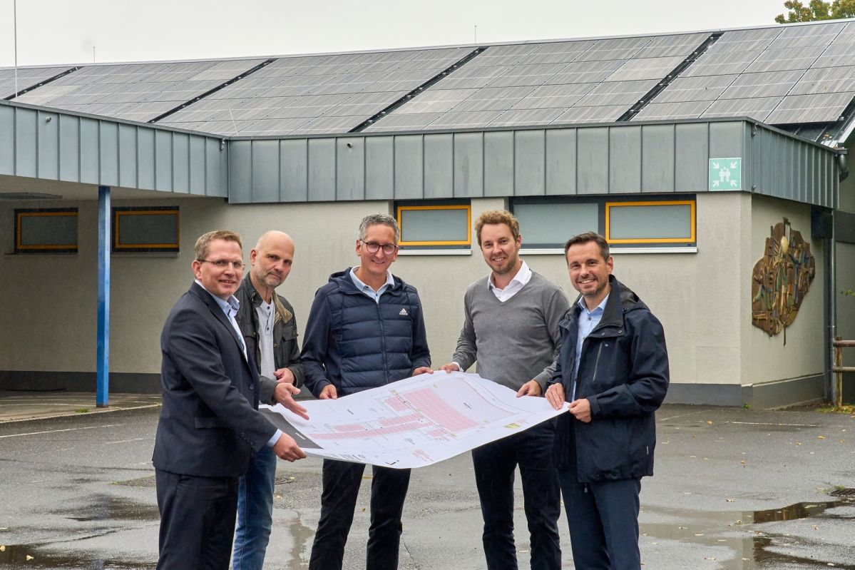 PV-Anlage GS Immendorf für KO-Solar Fünf Männer stehen auf einem Innenhof und halten eine Karte. Sie sind professionell gekleidet und lächeln freundlich.
