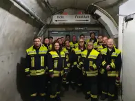 Eine Gruppe von Feuerwehrleuten in leuchtend gelben Uniformen steht vor einer grauen Tunnelwand.