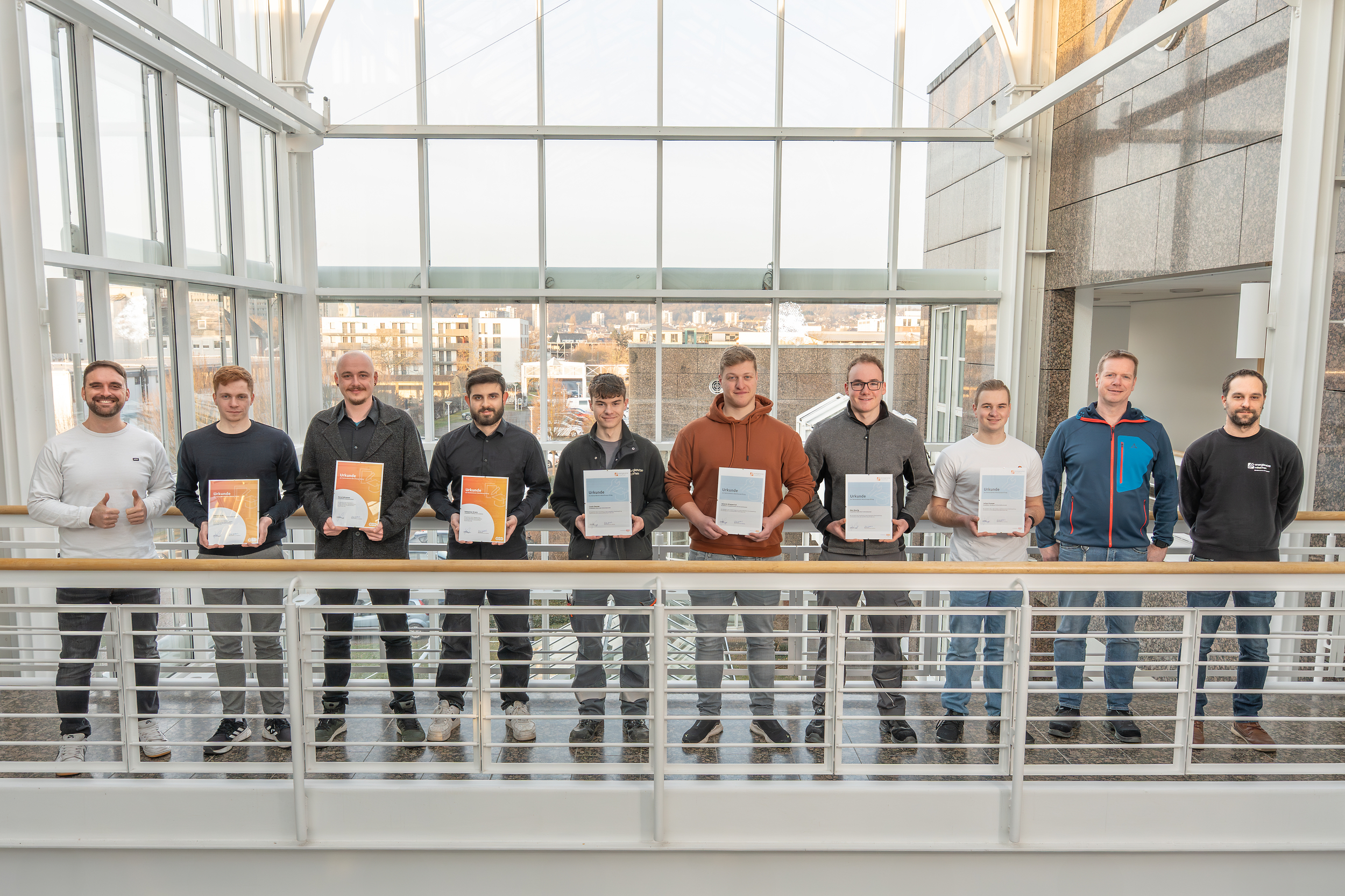 Zehn Männer stehen auf einer Balustrade und lächeln freundlich. Sieben von ihnen halten Urkunden in der Hand.