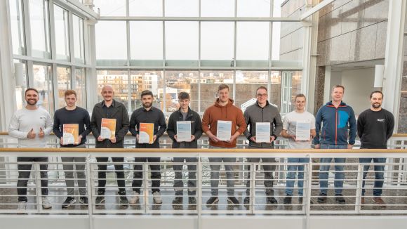 Zehn Männer stehen auf einer Balustrade und lächeln freundlich. Sieben von ihnen halten Urkunden in der Hand.