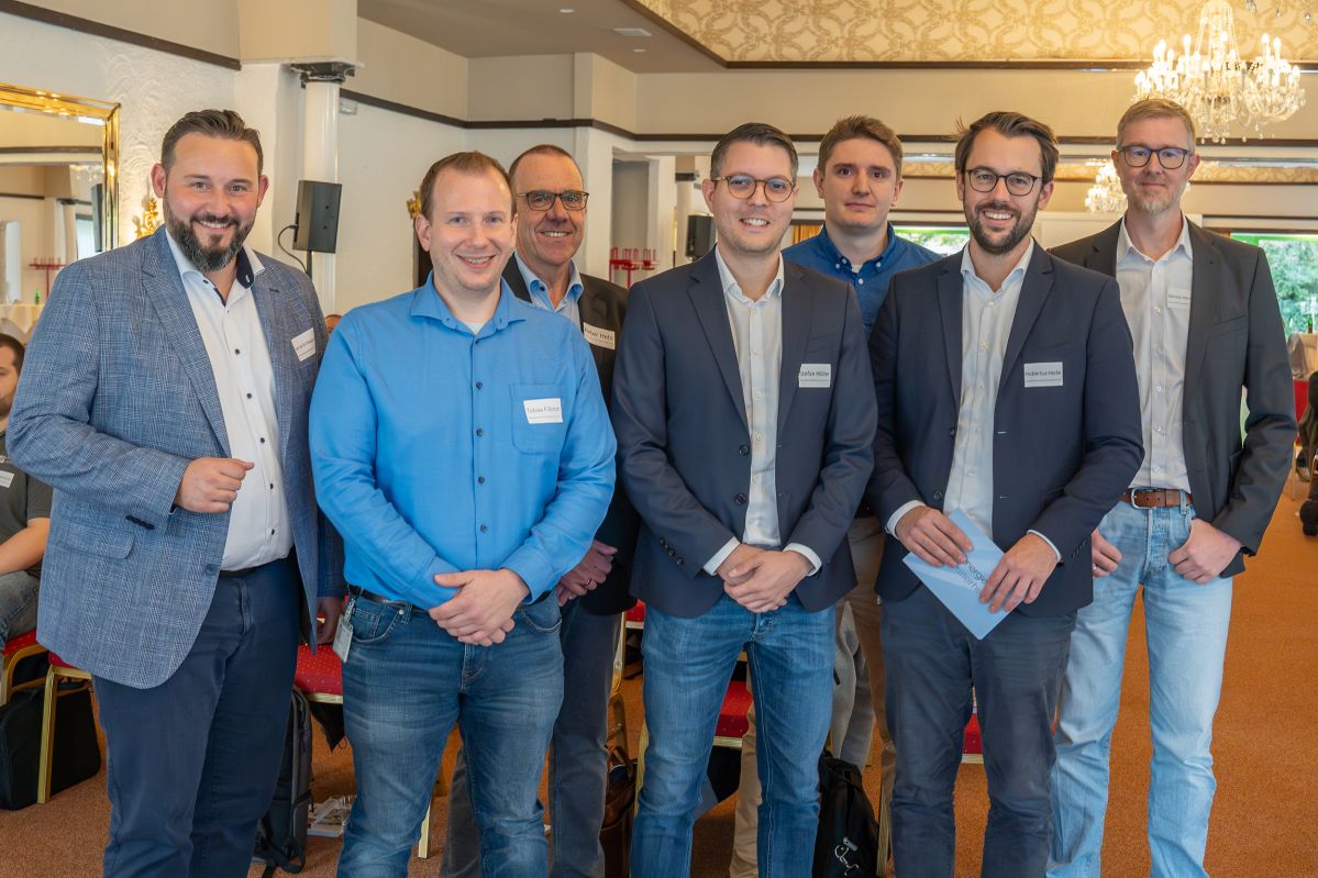 MP-Veranstaltung-21 Sieben professionell gekleidete Männer stehen in einem Vortragssaal und lächeln freundlich.