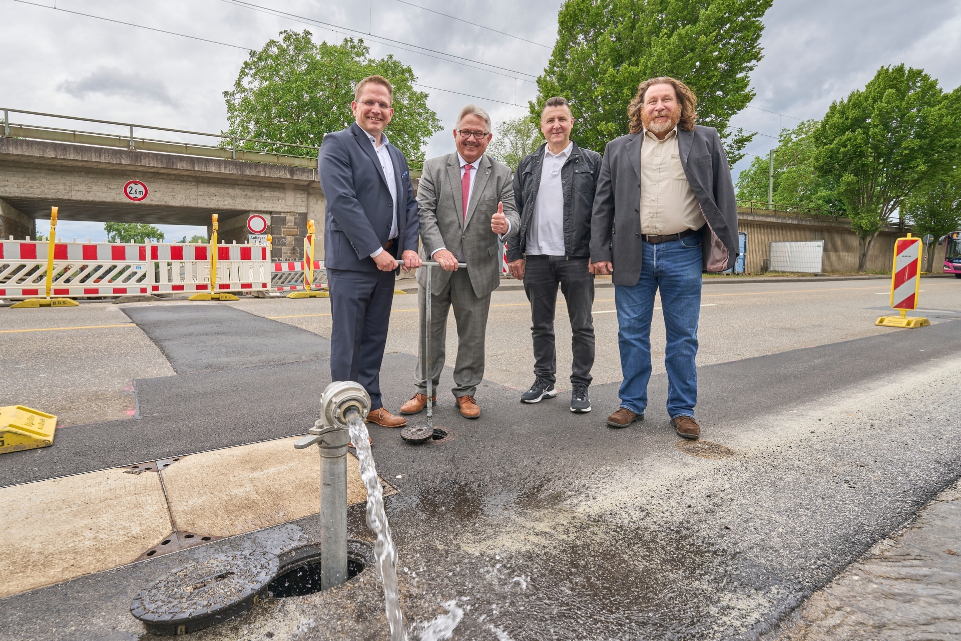 Vier professionell gekleidete Männer stehen vor einer Wasserleitung