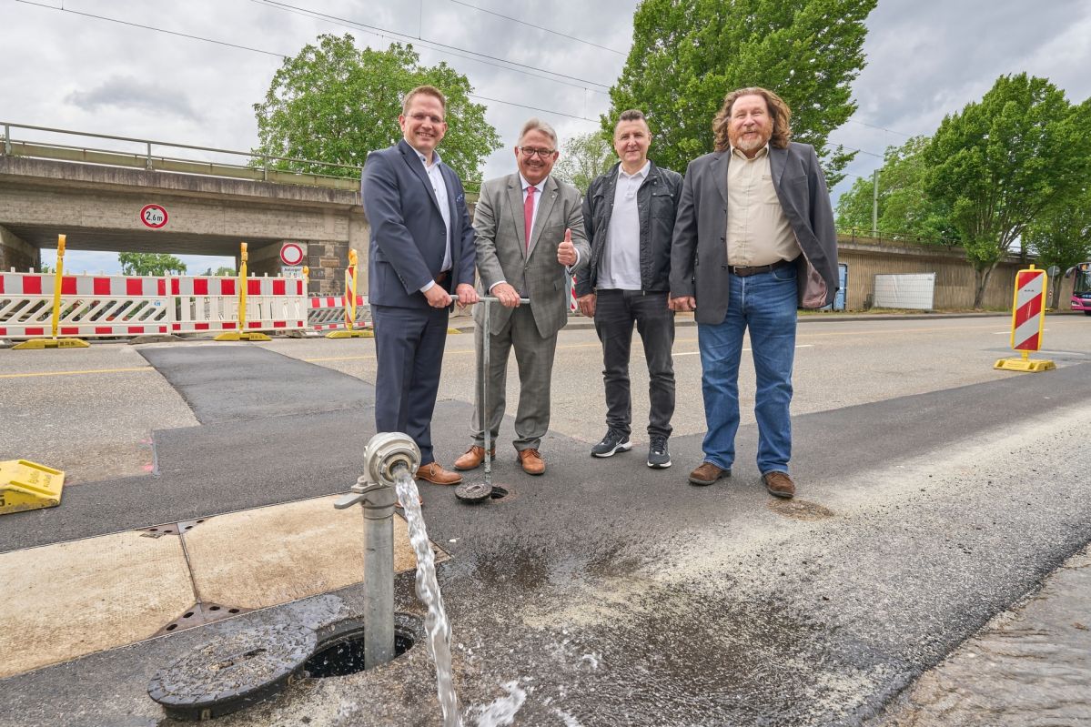Vier professionell gekleidete Männer stehen vor einer Wasserleitung