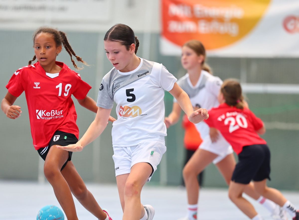 Vier Mädchen in roten Trikots und weißen evm Trikots spielen Handball in einer Sporthalle.